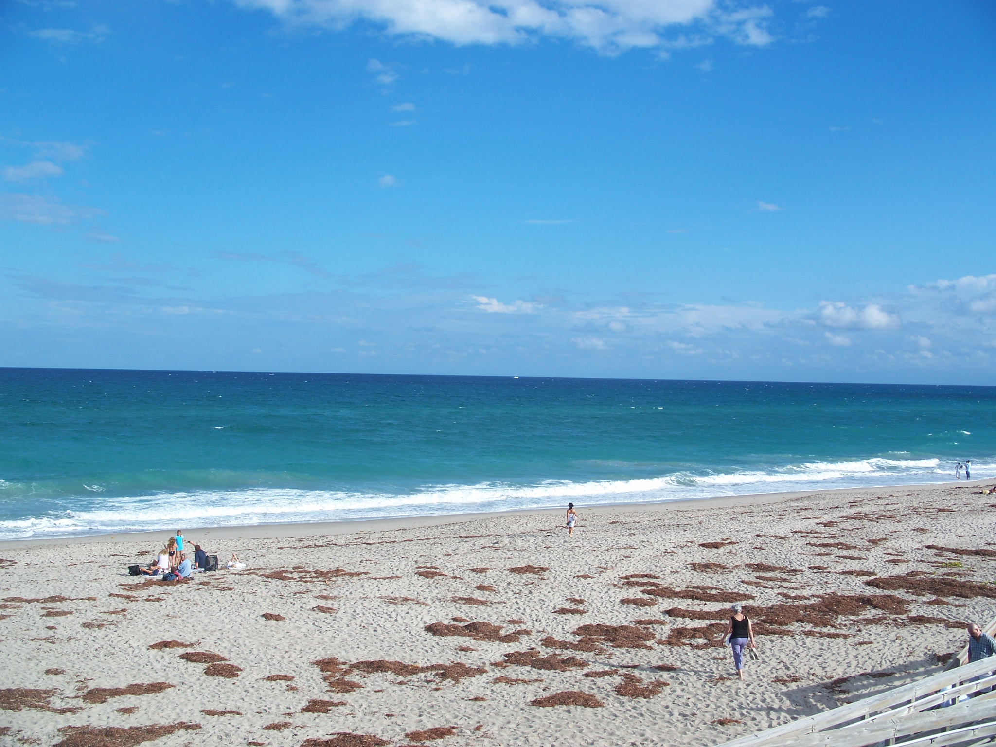 People walking along sandy beach with turquoise ocean waves