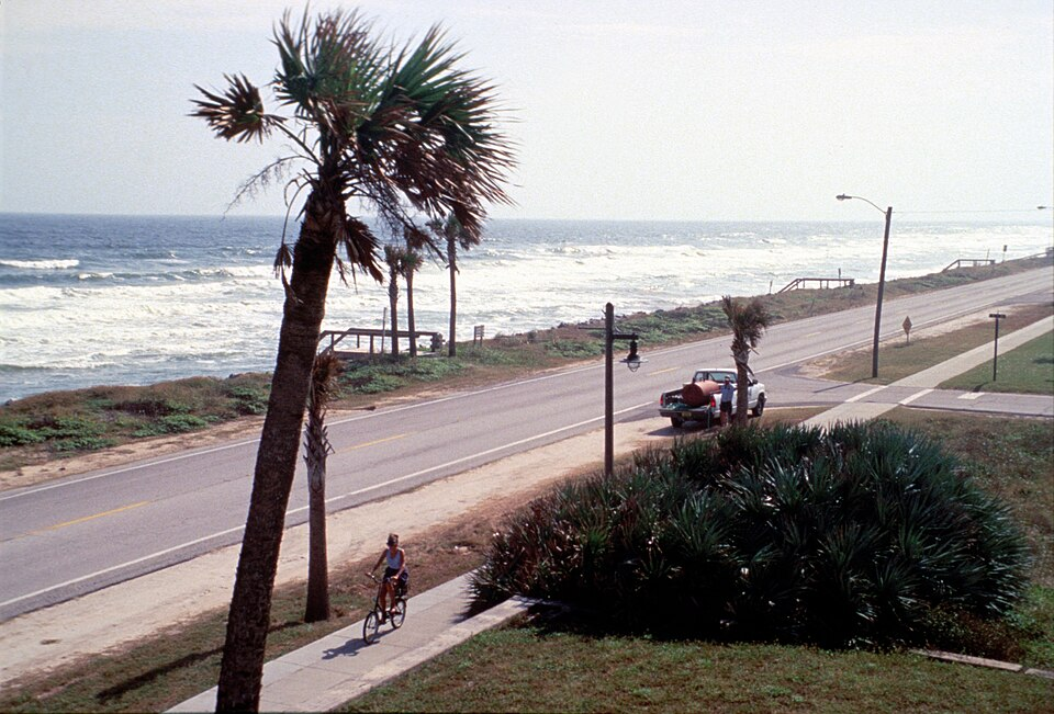 Cyclist riding along A1A coastal road beside ocean waves.