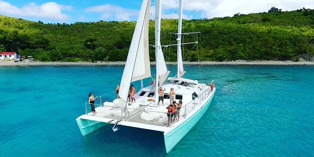 Catamaran party boat anchored in turquoise tropical waters with people on deck.