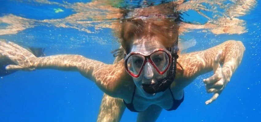 Snorkeler swimming underwater with mask in clear blue sea.
