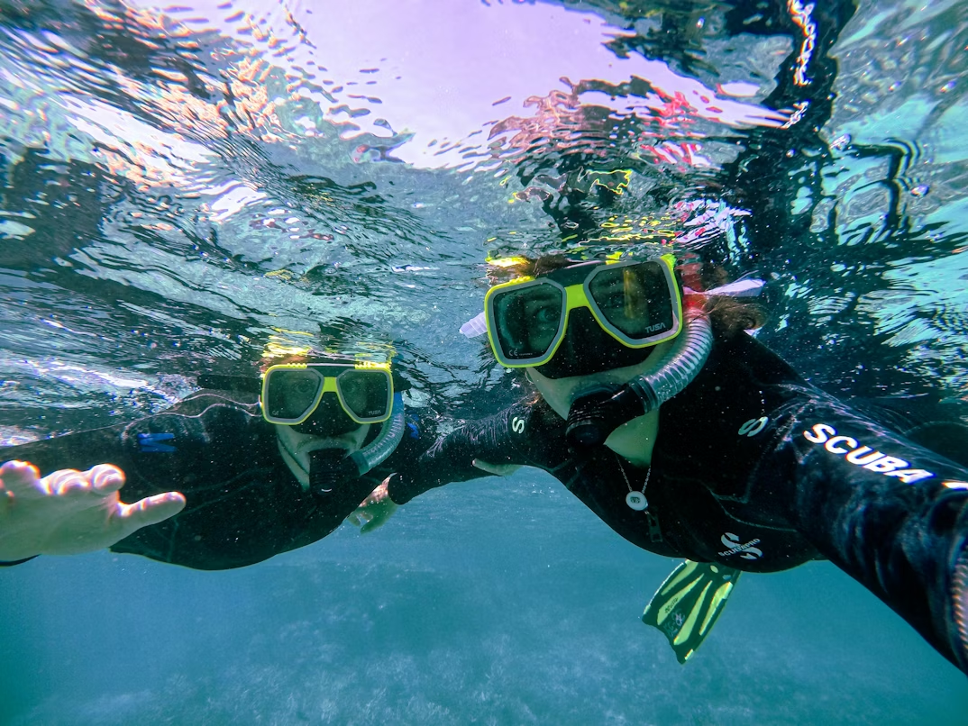 Two snorkelers swimming underwater above coral reef.