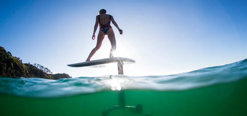 Surfer gliding above ocean waves on hydrofoil hoverboard.