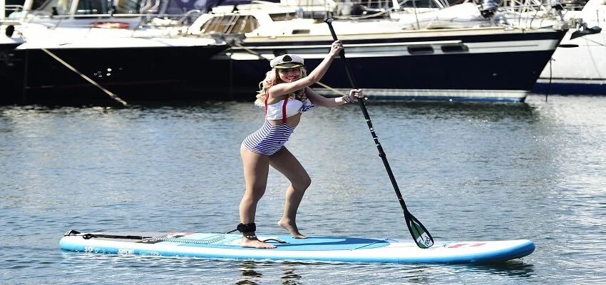 Person paddleboarding in a marina with yachts in background.