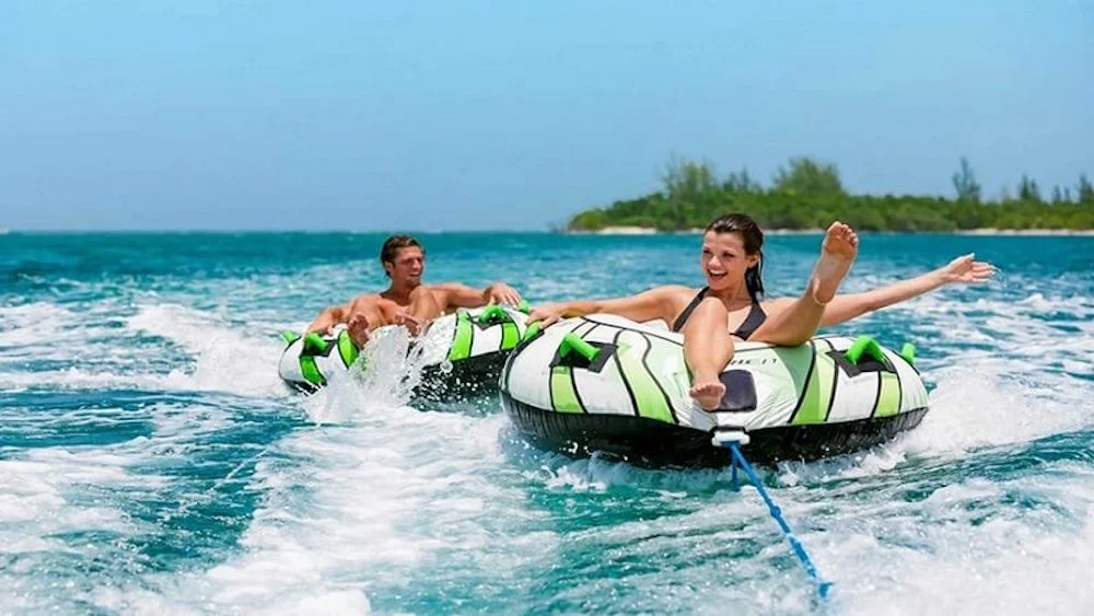 Two riders tubing on ocean waves near a tropical island.