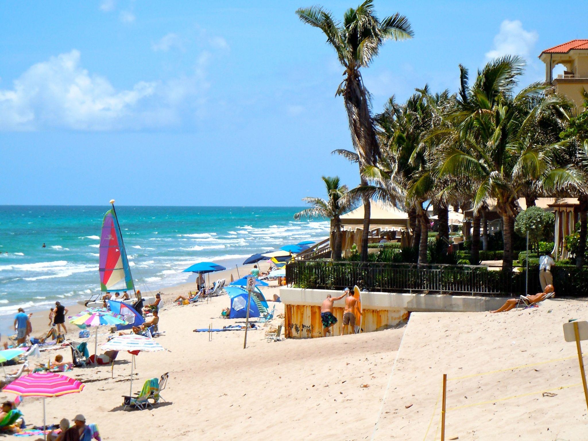 Beachgoers with umbrellas and sailboat at Lantana Beach.
