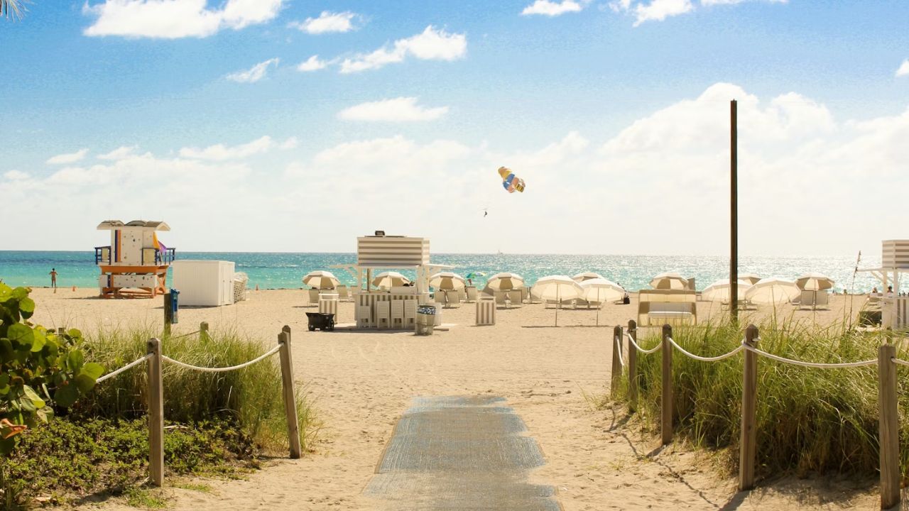 Sunny Florida beach with umbrellas, lifeguard tower, parasailer. 